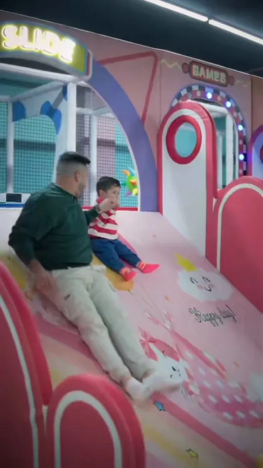 Padre e hijo bajando el tobogán rosa a la piscina de bolas